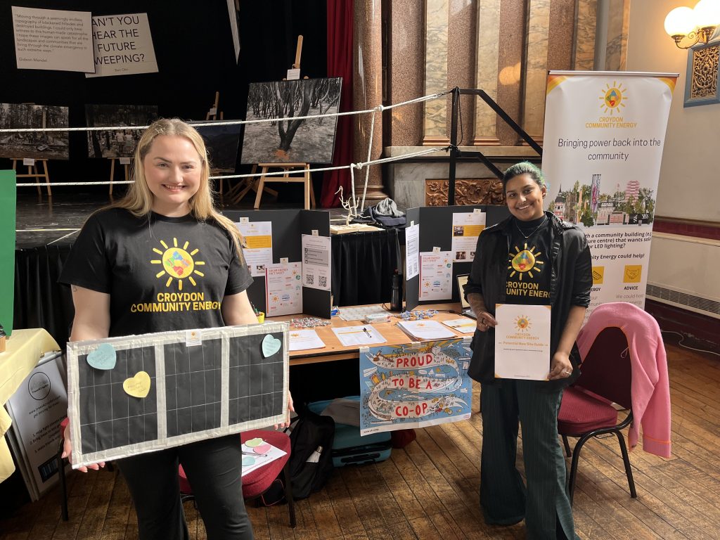 Two people standing in front of a stall holding signs about their community energy engagement event