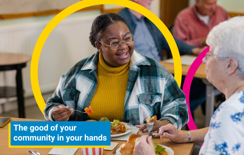 Smiling people enjoying a meal together in a community hub. A graphic reads 'the good of your community in your hands'.